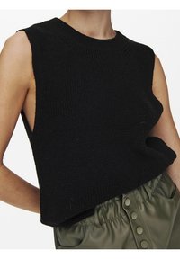 Black sleeveless knit top with a textured finish, featuring a round neckline and side slits; styled with green high-waisted pants.