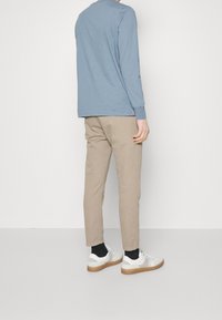 Jasnoniebieska koszula z długim rękawem, beżowe chinosy, białe trampki z gumowymi podeszwami. Prosty design, miękka faktura i neutralna kolorystyka.