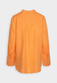 Camicia di lino arancione con colletto alla coreana, maniche lunghe e polsini con bottone. Presenta un dettaglio a pieghe lungo il retro per un'ulteriore texture.