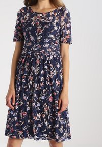 Marineblaues Kleid mit Blumenmuster und kurzen Ärmeln, gefertigt aus strukturiertem Stoff, mit tailliertem Oberteil und ausgestelltem Rock. Das Blumenmuster enthält rosa und blaue Akzente.