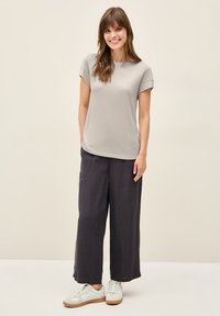 Lichtgrijze top met korte mouwen, gecombineerd met losse, donkergrijze wijde broek. Het model draagt witte sneakers met getextureerde tan accenten.