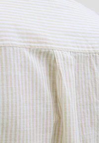 Camisa ligera a rayas con una paleta de colores beige y crema. Presenta una tela suave y texturizada, además de un diseño con pliegues en la parte posterior.