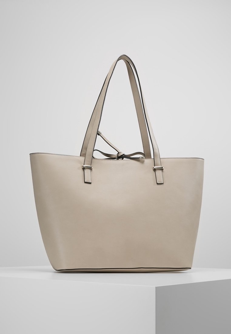 Beige læder tote taske med lange håndtag, struktureret form og et minimalistisk design. Har en knyttet lukning og diskrete syninger.