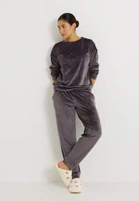 Ensemble de pyjama en velours gris avec une coupe décontractée, présentant un col rond et des motifs d'étoiles blanches éparpillées ; associé à des chaussons blancs moelleux.