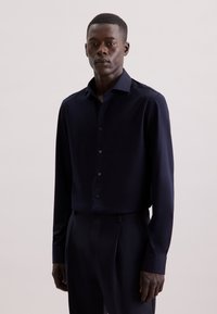Camicia a maniche lunghe blu navy realizzata in tessuto liscio, con colletto button-down e bottoni abbinati, abbinata a pantaloni scuri su misura.