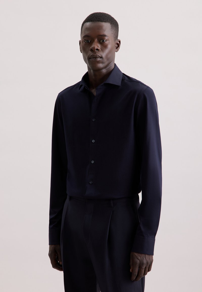 Camicia a maniche lunghe blu navy realizzata in tessuto liscio, con colletto button-down e bottoni abbinati, abbinata a pantaloni scuri su misura.