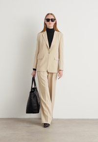 Beige tailored suit with a single-button blazer and wide-leg trousers, paired with a black turtleneck and oversized black tote bag.