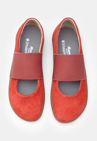 Zapatos planos rojos con un upper suave y texturizado, que cuentan con una amplia cinta elástica en la parte media del pie y una punta redondeada. Plantilla gris con marca.