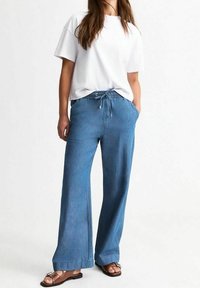 Široké světle modré džíny s elastickým páskem na šňůrku a bočními kapsami, kombinované s obyčejným bílým tričkem s krátkým rukávem.