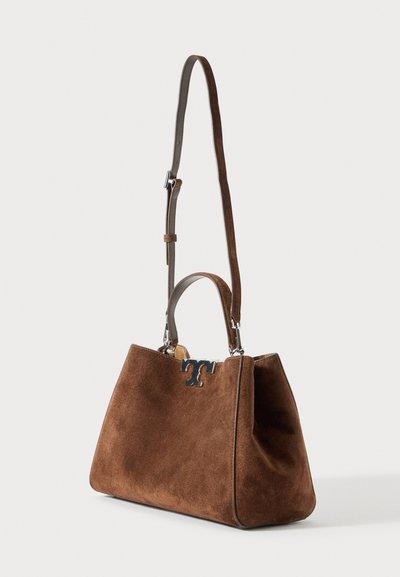 Bolsa de mão em camurça castanha com forma estruturada, fecho de logótipo prateado, alça curta e correia de ombro longa e ajustável sobre um fundo branco.