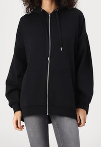 Svart zip-up hoodie gjord av en bomullsblandning med huva, långa ärmar, framfickor och detaljer med silverdragkedja. Slät textur, avslappnad passform.