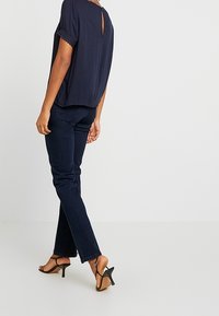 Navy short-sleeve top with a back keyhole, paired with dark blue jeans and black stiletto heeled sandals. Simple, relaxed design.
