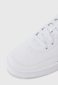 Baskets blanches avec une tige synthétique texturée, bout rond, laçage à l'avant, couture détaillée et perforations sur la boîte à orteils pour laisser passer l'air.