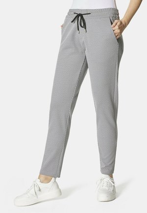 Black and white patterned sweatpants with an elastic waistband and drawstring. Features side pockets and tapered legs. Worn with white sneakers.