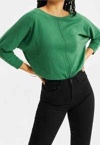 Grön långärmad topp med rund halsringning och sömdetaljer. Matchas med svarta högmidjade jeans med framfickor.