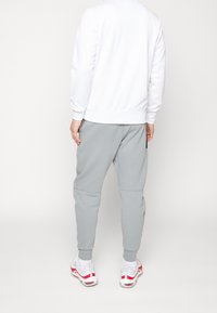 Vit sweatshirt och grå joggers med elastiska muddar och midja. Joggers har dragkedjefickor, slät yta och avslappnad passform.