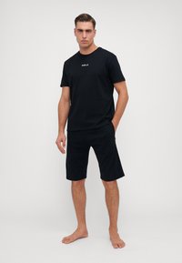 Camiseta de algodón negra de manga corta con el logo "REPLAY", combinada con pantalones cortos negros a juego, ambos con un ajuste relajado.