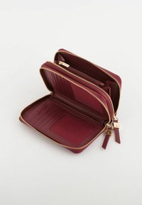 Portefeuille bordeaux zippé avec ferrures dorées, emplacements pour cartes à l'intérieur et une fenêtre transparente pour la carte d'identité. Extérieur texturé et doublure lisse.