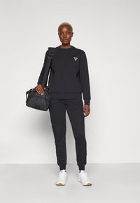 Completo felpa nera e pantaloni jogger, in misto cotone, con logo sul petto, polsini a costine e una borsa a secchiello nera con trama.