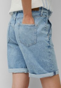 Světle modré džíny šortky s uvolněným střihem, ohrnovacími manžetami a dvěma zadními kapsami. Materiál má mírnou texturu a vybledlý vzhled.