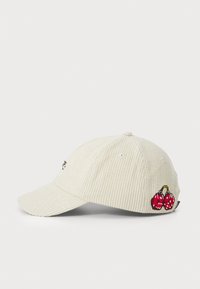Corduroy baseball cap in cream with a curved brim, featuring embroidered red cherries with white polka dots and ventilation eyelets.