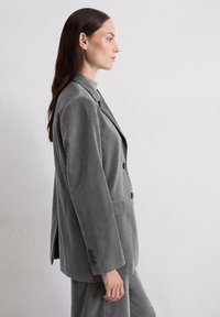 Gray corduroy blazer with two buttons, notch lapel, and side pockets. The fabric has a soft texture, creating a sleek silhouette.