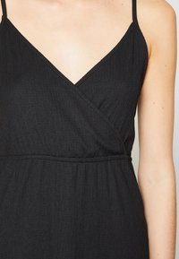 Robe noire avec décolleté en V et bretelles spaghetti ajustables. Le tissu présente un design texturé et froissé avec une taille élastique.