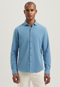Camicia azzurra a maniche lunghe realizzata in tessuto morbido, con chiusura frontale a bottoni, colletto e un sottile logo ricamato sul petto.