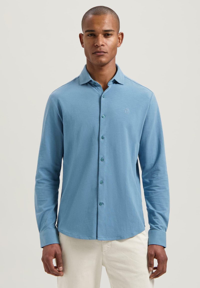 Camicia azzurra a maniche lunghe realizzata in tessuto morbido, con chiusura frontale a bottoni, colletto e un sottile logo ricamato sul petto.