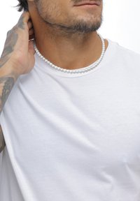 Vit t-shirt med en slät textur, prydd med ett pärlhalsband runt halsen, som visar runda, glansiga vita pärlor.