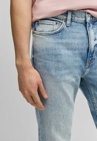 Jeans de mezclilla azul claro con un acabado desgastado, que presentan un diseño de cinco bolsillos y una etiqueta de marca visible en la parte trasera de la cinturilla.