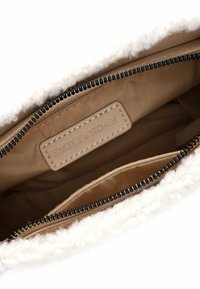 Interno della borsa beige con un morbido bordo in pelliccia bianca, chiusura a zip e un'etichetta che reca la scritta "EMILY & NOAH." Presenta un rivestimento liscio e texturizzato.