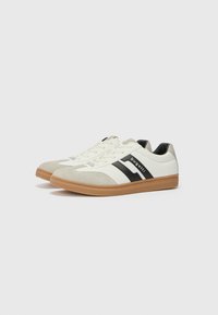 White and gray sneakers with black stripes, suede and leather materials, round toe, and gum rubber sole. Brand name on the side.
