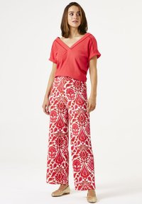 Suéter coral con escote en V y mangas cortas enrolladas, combinado con pantalones de pierna ancha que presentan un patrón floral en rojo y rosa. Bailarinas beige.