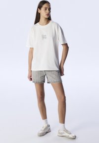 Camiseta de algodón blanca con mangas cortas y un pequeño estampado gráfico en el pecho, combinada con pantalones cortos a rayas grises y zapatillas de color claro.