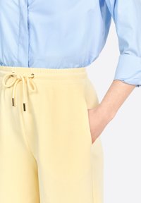 Yellow pants with an elastic waistband and drawstring, featuring side pockets. Paired with a light blue, collared shirt. Smooth texture.