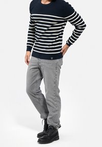 Sweter w paski granatowo-białe wykonany z dzianiny z okrągłym dekoltem, zestawiony z szarymi dżinsami denimowymi i czarnymi sznurowanymi butami, wykonany z tkaniny o fakturze.