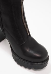 Bottine en cuir noir avec semelle épaisse à crampons et fermeture éclair argentée visible sur le côté.