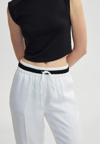 Zwart cropped top gecombineerd met witte, ruime broek met elastische tailleband en koord. Glad weefsel met een subtiele glans.