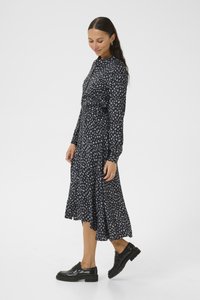 Navy-blaues langärmeliges Kleid mit taillierter Taille und ausgestelltem Rock. Verfügt über einen kleinen Kragen und ein weißes Blättermuster. Getragen mit schwarzen Plateauschuhen.