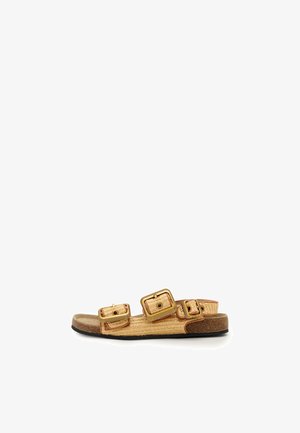 Sandale plată cu trei curele late bej ajustabile, prevăzute cu catarame mari pătrate aurii și talpă de plută cu talpă neagră.