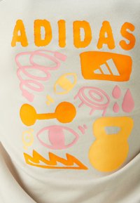 Beige ruházat élénk narancssárga és rózsaszín nyomtatott grafikákkal, köztük az "ADIDAS" szóval és különböző sporttal kapcsolatos ikonokkal.