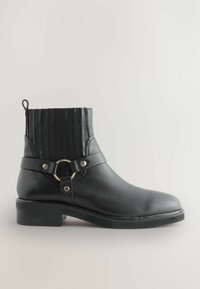 Botín negro de cuero hasta el tobillo con lado elástico acanalado, acento de hardware dorado circular y tacón bajo. Textura suave con un diseño elegante.