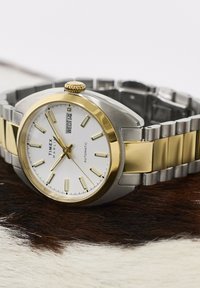 Automatické hodinky Timex Marlin so zlatým a strieborným kovovým remienkom, bielym ciferníkom, zlatými hodinovými značkami a zobrazením dňa a dátumu s údajom streda 14.