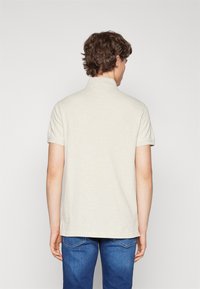 Polo shirt in cotone beige con colletto, maniche corte e orlo dritto. Il modello indossa jeans in denim blu, visto da dietro.