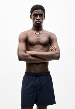 Pantaloni da bagno blu navy con vita elastica e cordoncino. Il modello ha un fisico muscoloso, le braccia incrociate, indossa una collana e non ha la maglietta.