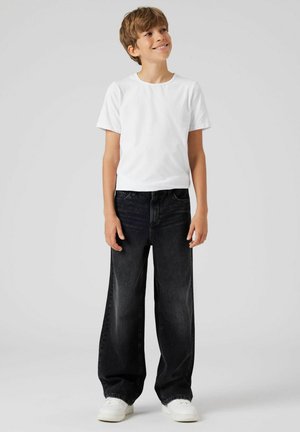 Witte korte mouw t-shirt gecombineerd met ruime, donkere jeans en witte sneakers. De stof is glad met een klassieke snit en rechte pijpen.