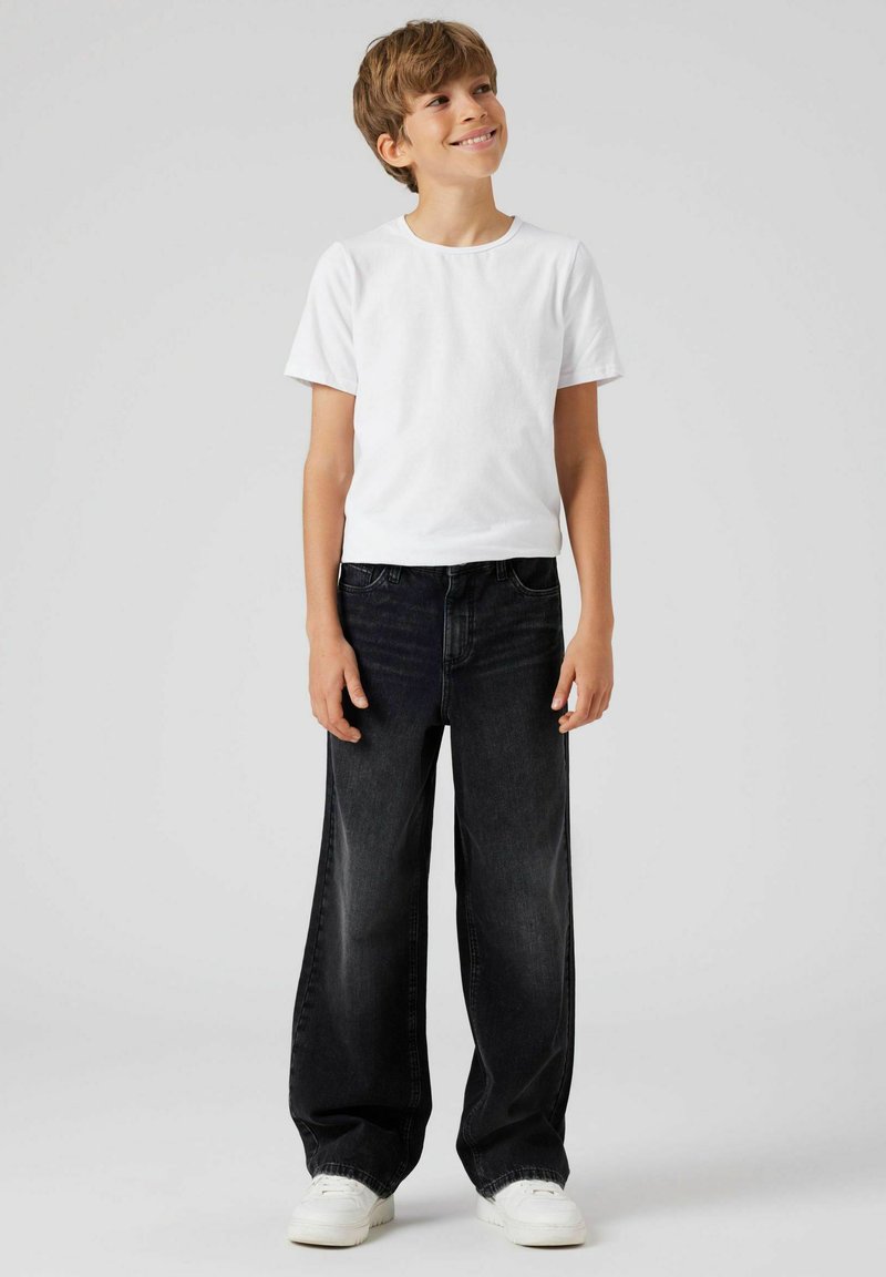T-shirt blanc à manches courtes assorti à un jean sombre ample et des baskets blanches. Le tissu est lisse avec une coupe classique et une jambe droite.