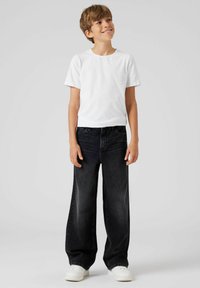 White short-sleeve t-shirt and loose-fitting black jeans with subtle fading. Completed with white sneakers on a neutral background.