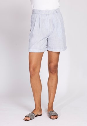 Light gray high-waist shorts with front pleats, cuffed hems, worn with black-and-white woven open-toe slide sandals.
